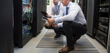 537445378-612x612 Computer technicians holding digital tablet while analysing server machines in server room.